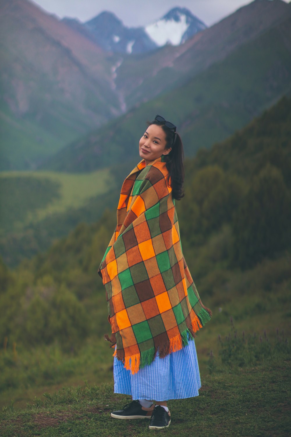 a woman standing in a field with mountains in the background