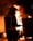 A firefighter in protective gear stands in front of a large, outdoor fire, holding a hose. The flames illuminate the scene, creating an intense and urgent atmosphere.