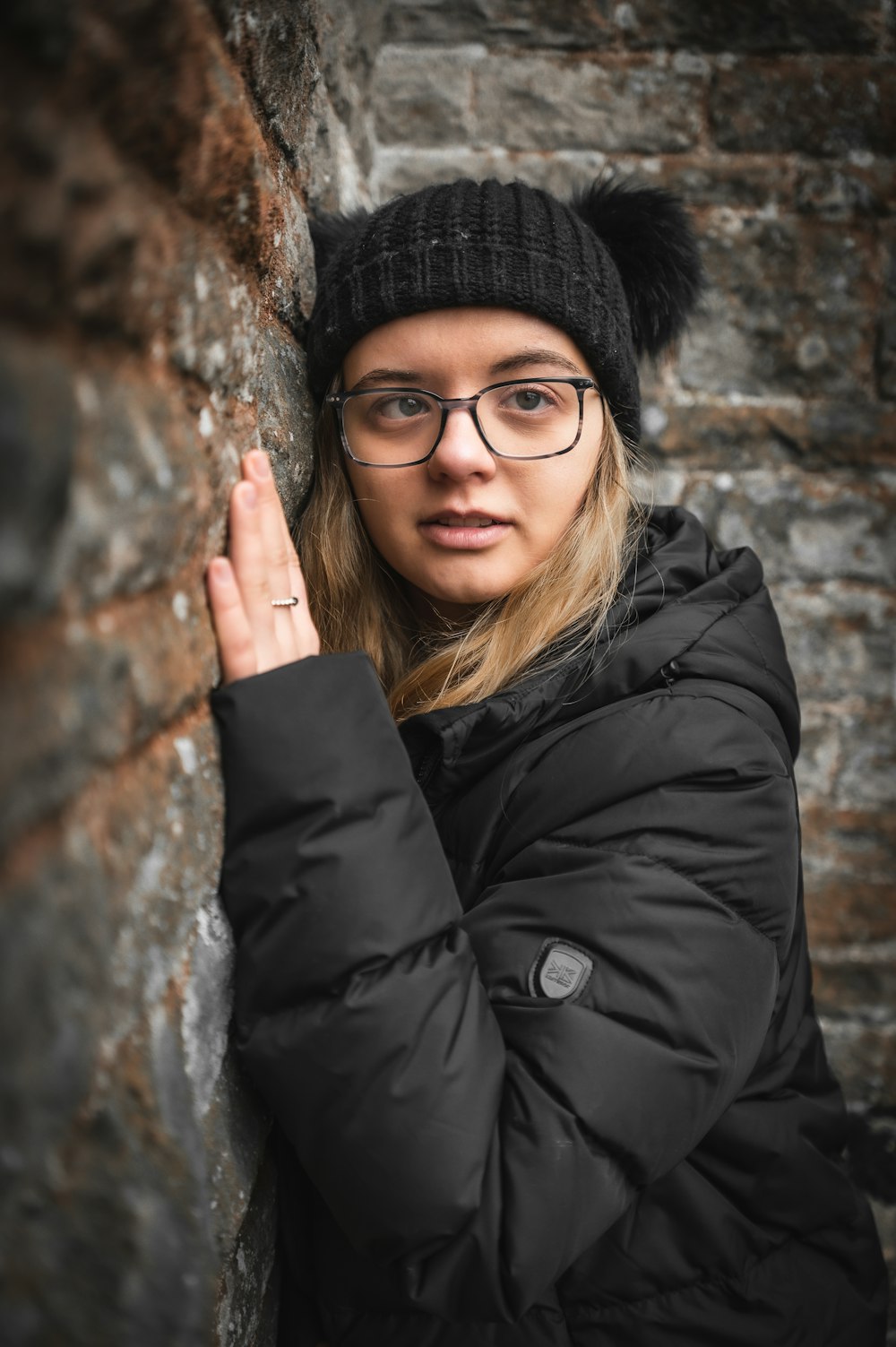 a woman wearing glasses leaning against a stone wall
