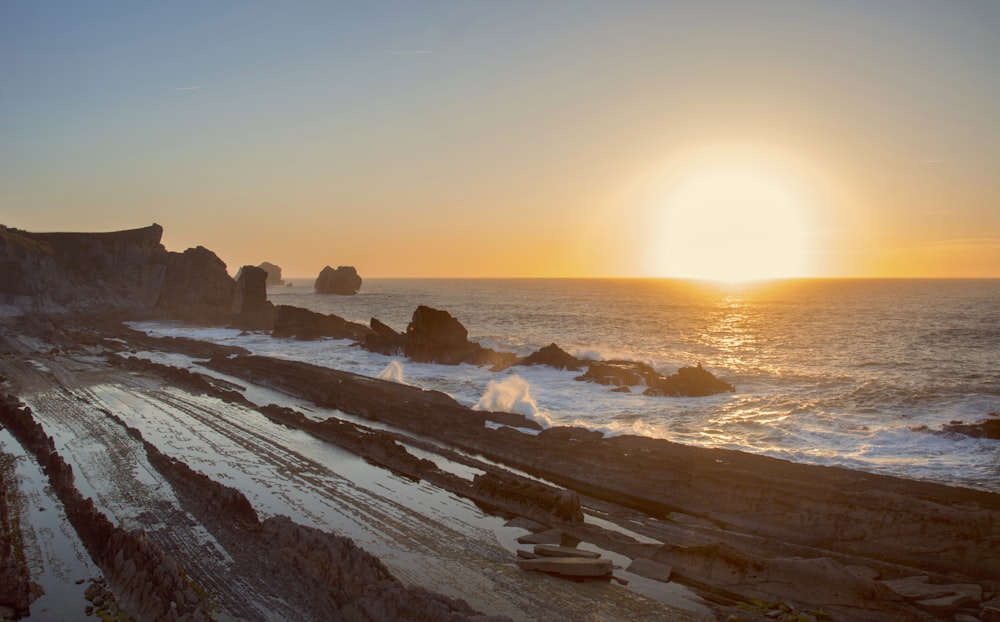 the sun is setting over a rocky beach