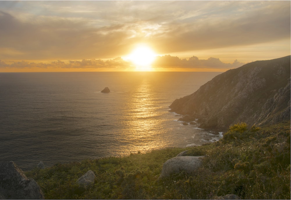 the sun is setting over the ocean on a cliff