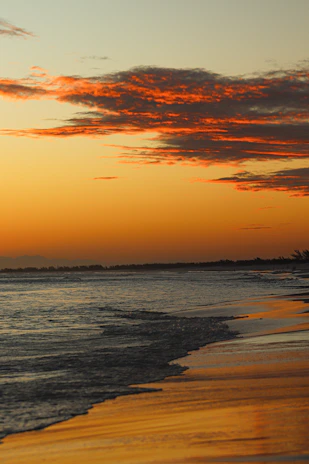 A serene beach at sunset with golden sand and calm waves reflecting the orange sky.