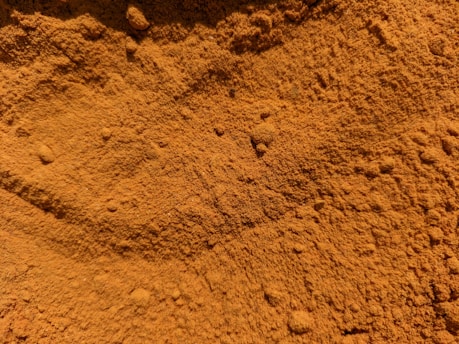 Close-up of vibrant orange peel powder spilling from a rustic wooden bowl onto a natural linen cloth.