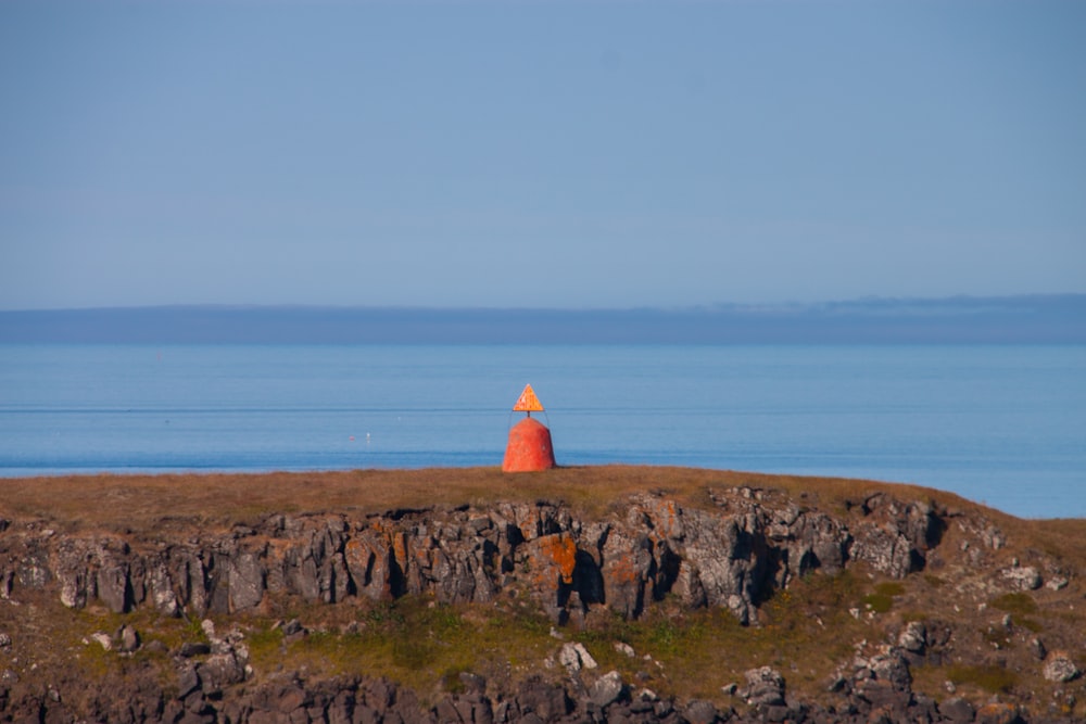an orange buoy sitting on top of a hill near the ocean