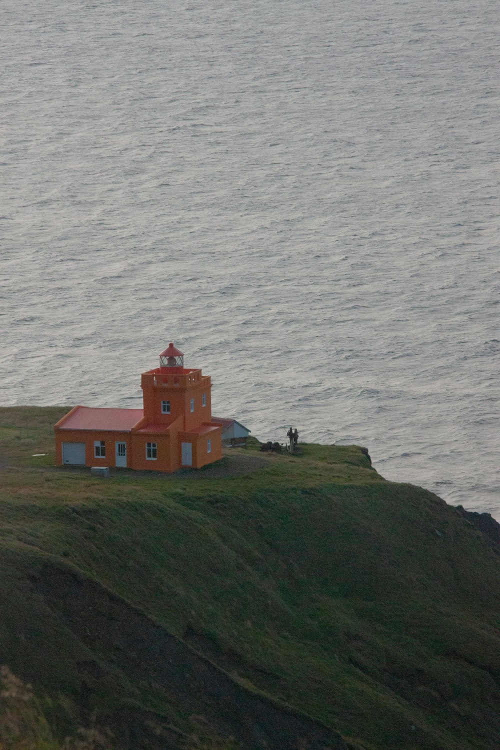 a small orange building sitting on top of a hill next to the ocean