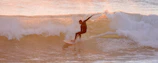 Surfer catching a perfect wave at sunrise with Mastrimersil gear