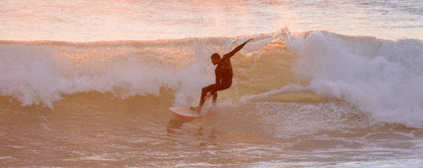A surfer riding a sleek evergrom surfboard at sunset, waves glowing orange.