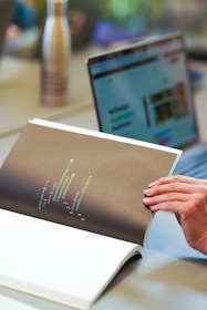 a person holding a book with a laptop in the background