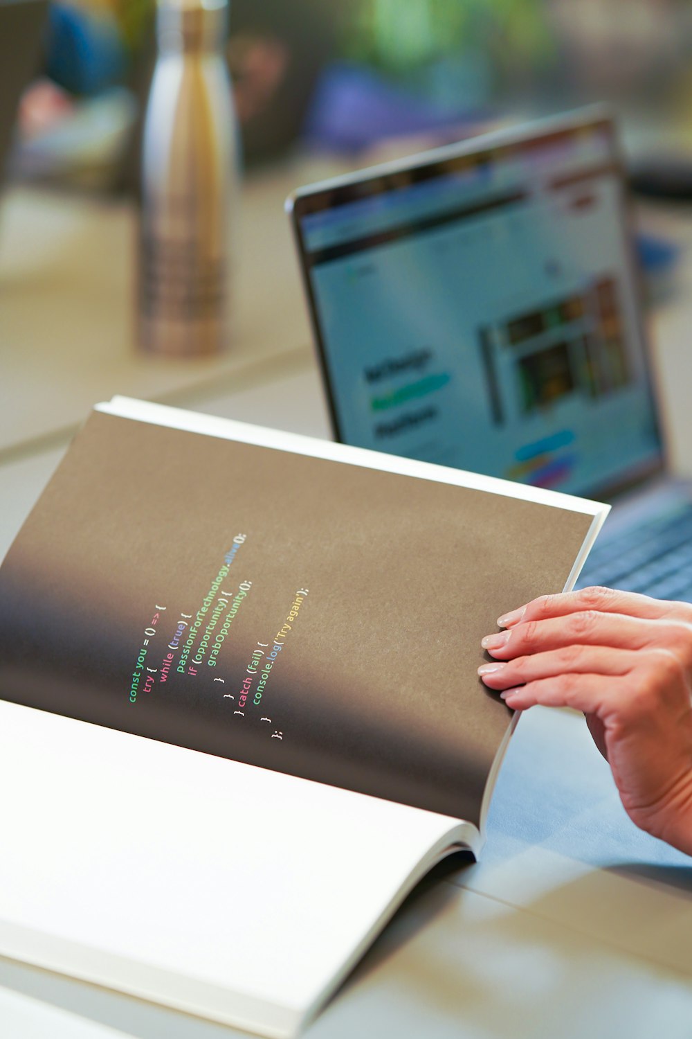 a person holding a book with a laptop in the background