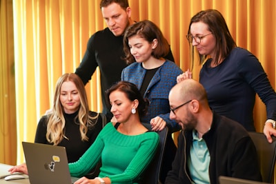 A vibrant office scene showing a diverse group of professionals collaborating around a laptop.