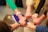Several people form a circle, joining their fists together in a gesture of unity and teamwork. Various wristwatches and clothing styles are visible, suggesting a diverse group.