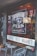 A storefront window displays the signage for 'Washington Perk and Provision Co.', featuring a graphic of a coffee cup. The interior appears warmly lit with hanging lights and decorative elements inside. Outside, there is a small seating area with two metal chairs and a round table.