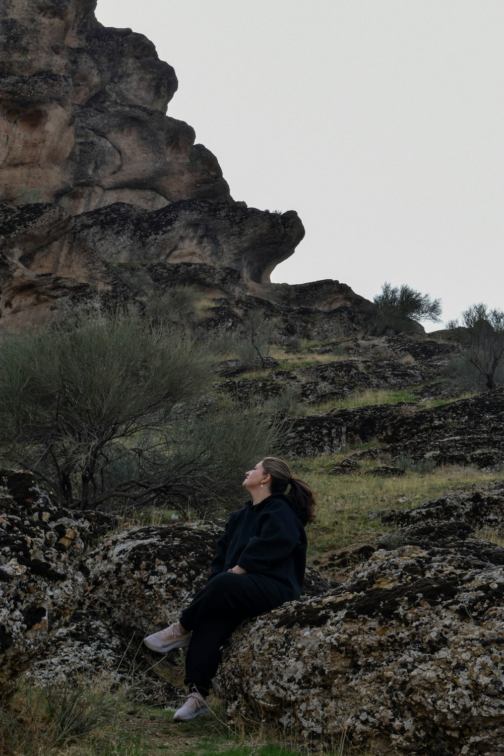 a woman sitting on a rock looking up into the sky