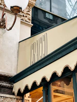 An elegant storefront with intricate architectural detailing, featuring a decorative lamp and a stylish sign with the word 'Cracco'. The building materials include ornate stonework and glass.