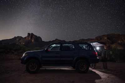 A sleek black SUV parked under a starry desert sky, ready for a long journey.
