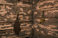 Two bundles of dried herbs are hanging on the rustic wooden walls, which have a distressed and weathered appearance with peeling paint and visible texture.
