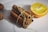 A bundle of cinnamon sticks tied with a string is placed next to a halved orange on a light-colored surface. The arrangement creates a contrast between the rich brown tones of the cinnamon and the vibrant yellow of the orange flesh.
