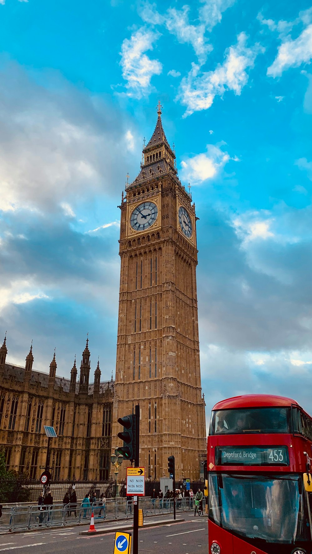 a red double decker bus driving past a tall clock tower