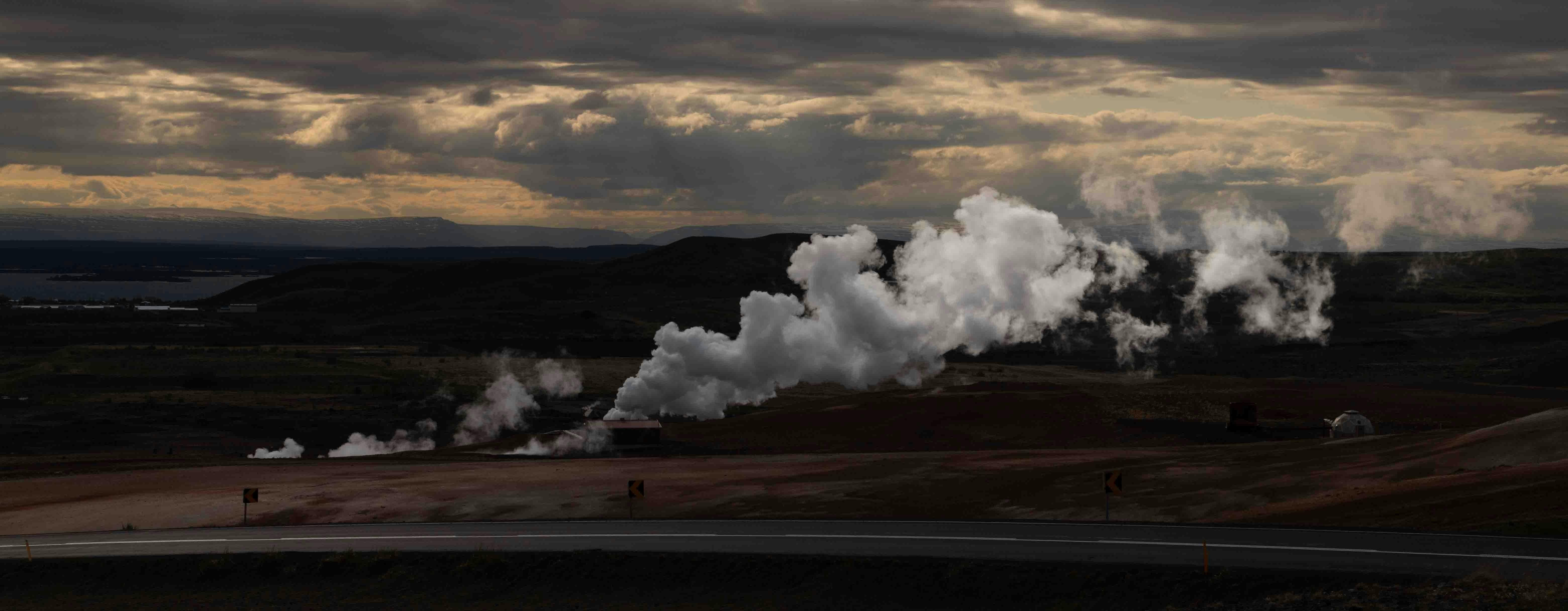 An evocative landscape under a moody sky, with geothermal steam vents releasing plumes of steam into the air, highlighting nature's energy