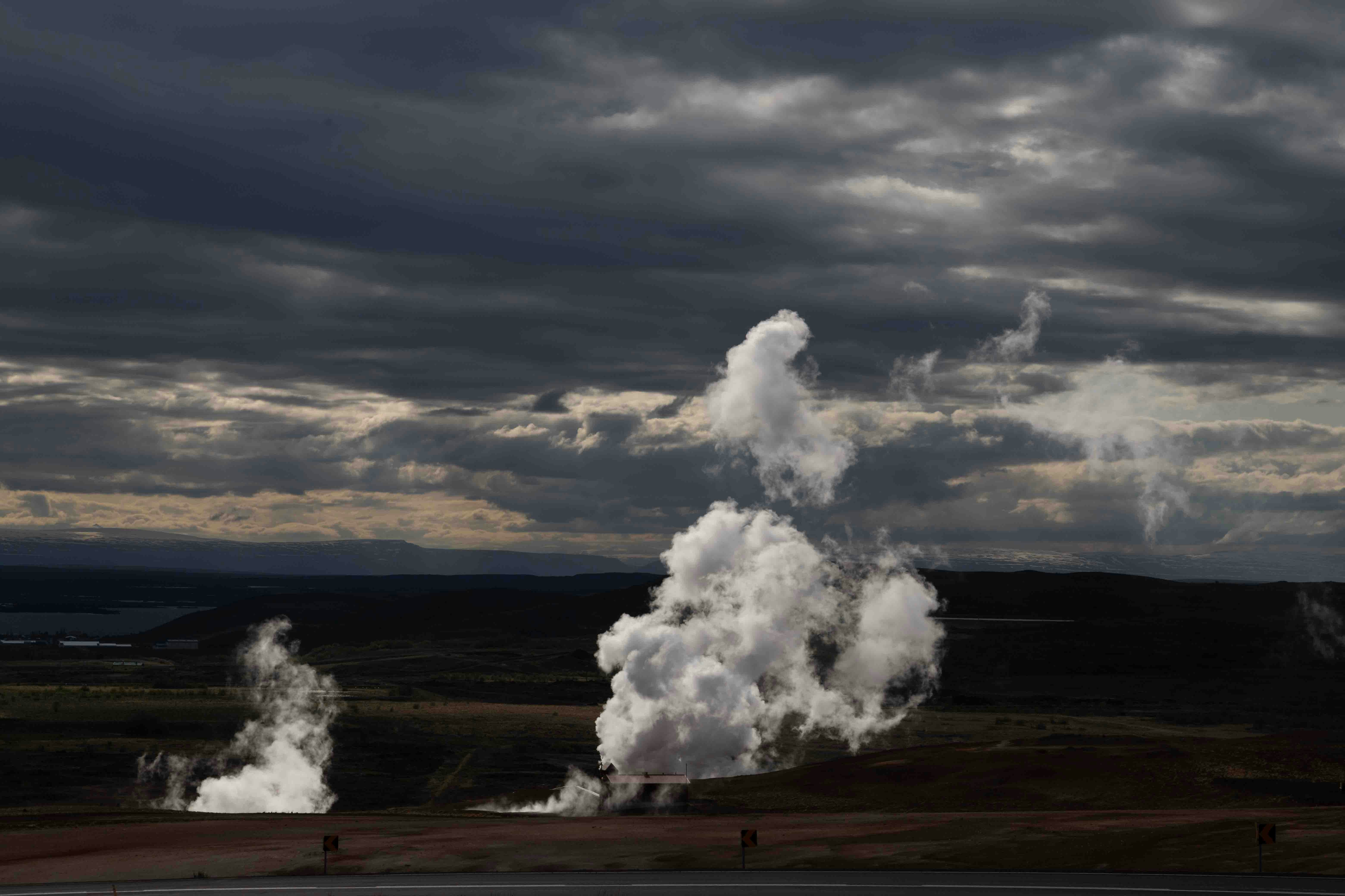 An evocative landscape under a moody sky, with geothermal steam vents releasing plumes of steam into the air, highlighting nature's energy