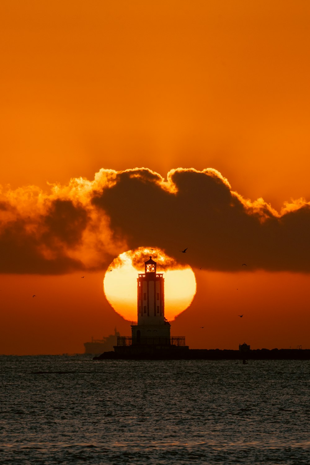 the sun is setting behind a lighthouse in the ocean