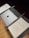 A music stand holds a closed laptop with an apple logo, a baton, and sheet music titled 'Troisième Symphonie' by Pierre Wissmer. The stand is set on a wooden floor.