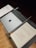 A music stand holds a closed laptop with an apple logo, a baton, and sheet music titled 'Troisième Symphonie' by Pierre Wissmer. The stand is set on a wooden floor.