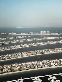 Aerial view of a series of narrow, man-made islands with numerous residential buildings. Each island is surrounded by water, resembling palm fronds radiating in a pattern. In the background, the calm sea extends to the horizon.
