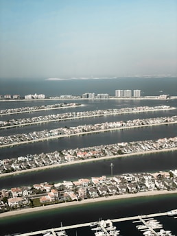 Aerial view of a series of narrow, man-made islands with numerous residential buildings. Each island is surrounded by water, resembling palm fronds radiating in a pattern. In the background, the calm sea extends to the horizon.