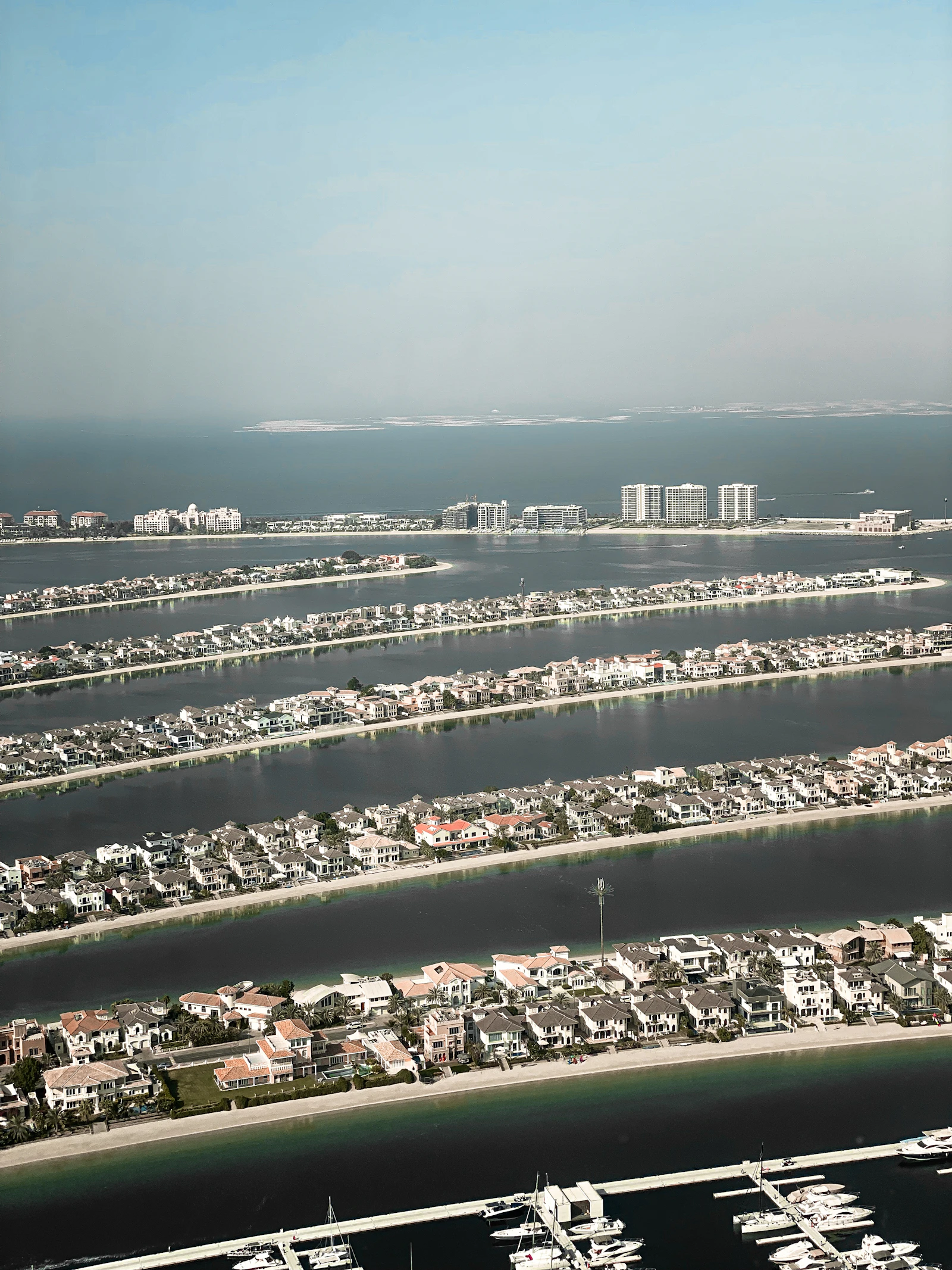Elevated view down the parallel Palm Jumeirah fronds packed with waterfront villas, with a marina and yachts in the foreground