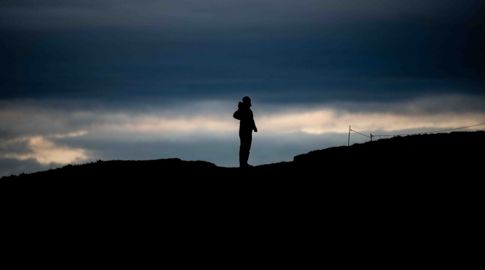 una persona de pie en la cima de una colina bajo un cielo nublado