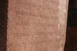 Close-up of sandstone tablets engraved with ancient Sanskrit scripts under warm ochre light.