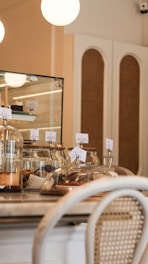 A cozy café interior with a countertop displaying assorted pastries under glass domes. Warm lighting and a mix of wooden and wicker furniture create a welcoming atmosphere.