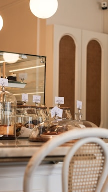 A cozy café interior with a countertop displaying assorted pastries under glass domes. Warm lighting and a mix of wooden and wicker furniture create a welcoming atmosphere.