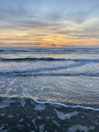 A serene Maldivian beach at sunrise with gentle waves and palm trees swaying.