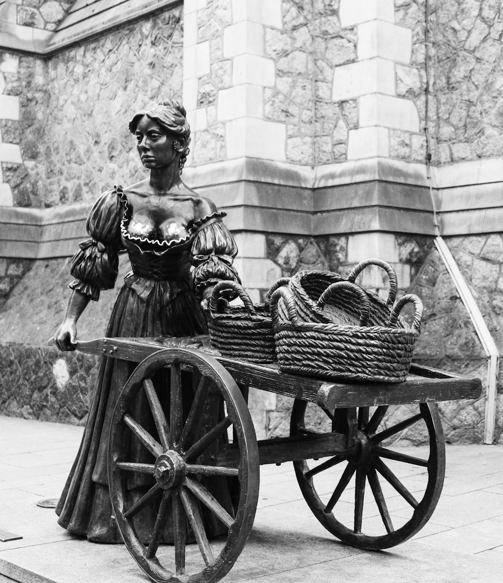 a black and white photo of a statue of a woman pushing a wagon