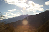 Sunlight filtering through solar panels with a backdrop of mountains and blue sky.