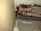 A close-up view of a section of an interior corner, where a wooden surface meets another wall. There appears to be significant dark brown mold or mildew growth covering portions of a peeling, textured surface. The area looks aged and deteriorated, with various shades of brown and beige.