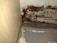 A close-up view of a section of an interior corner, where a wooden surface meets another wall. There appears to be significant dark brown mold or mildew growth covering portions of a peeling, textured surface. The area looks aged and deteriorated, with various shades of brown and beige.