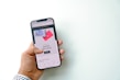 A hand is holding a smartphone displaying a screen with an advertisement for Airbnb gift cards. The screen shows a shopping option and imagery of gift cards against a bright background.