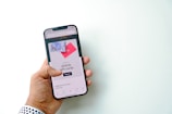 A hand is holding a smartphone displaying a screen with an advertisement for Airbnb gift cards. The screen shows a shopping option and imagery of gift cards against a bright background.