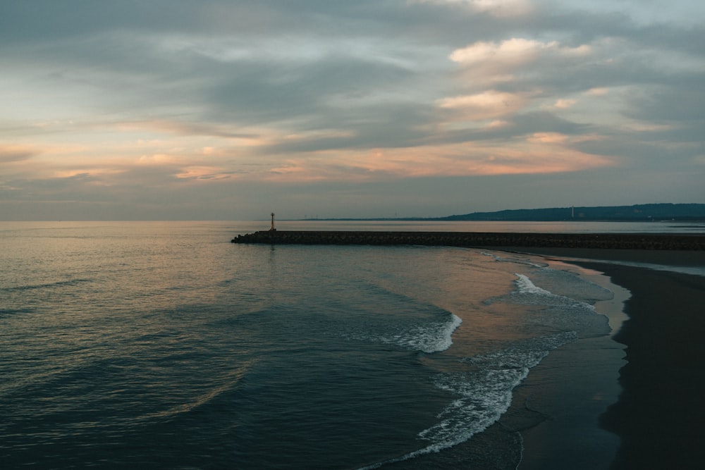 a body of water sitting next to a beach under a cloudy sky