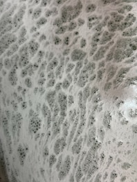 A close-up view of white foam with numerous small bubbles on the surface, creating a textured pattern reminiscent of soap suds.
