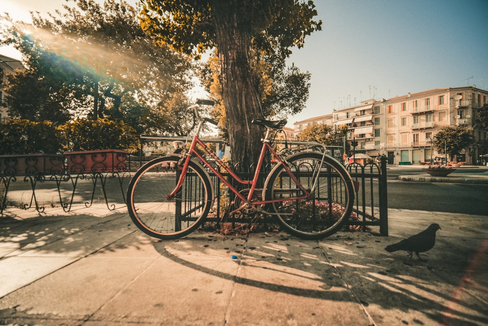 a red bike parked next to a tree on a sidewalk