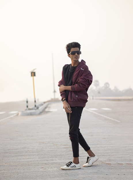 A confident young person wearing a vibrant streetwear jacket and sneakers, walking through an urban cityscape.