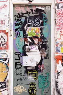 A door covered in vibrant graffiti and stickers, including various artistic designs and messages such as 'Don't agree to their terms & conditions' and 'This is for you.' The numbers '4 9' are prominently displayed, along with cartoon-like characters and colorful illustrations. Surrounding the door are more layers of urban street art and posters.