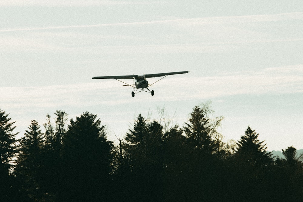 a small plane flying over a forest under a cloudy sky