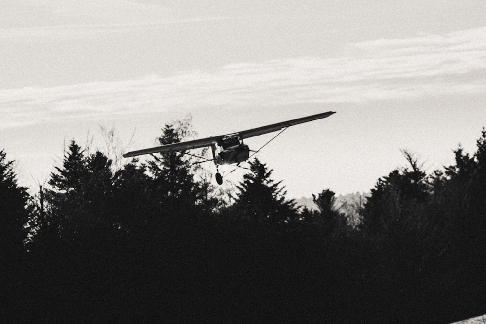 a small airplane flying over a forest filled with trees