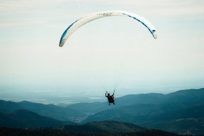 Paraglider soaring above the green hills of Poggio Bustone under a clear blue sky.