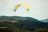 Adventurers paragliding over the lush green hills.